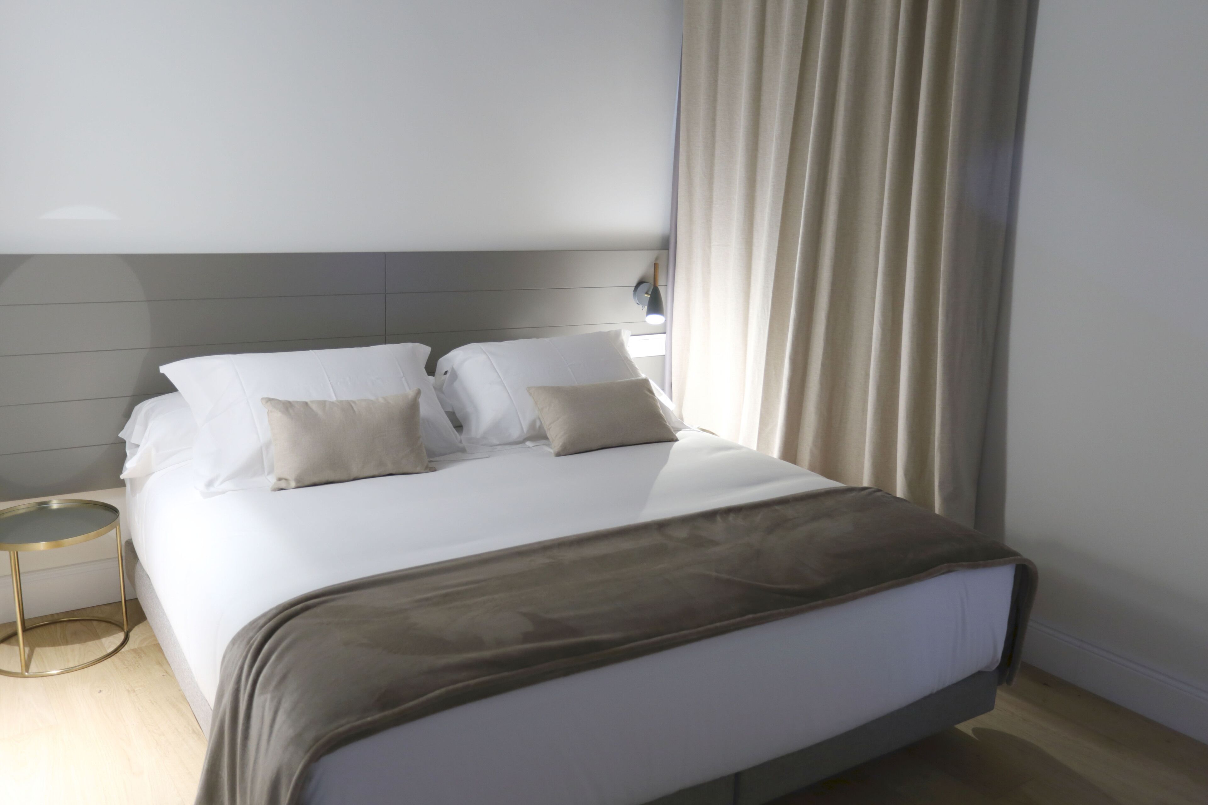 Una habitación de hotel moderna con una cama grande, una mesita de noche y una cortina.