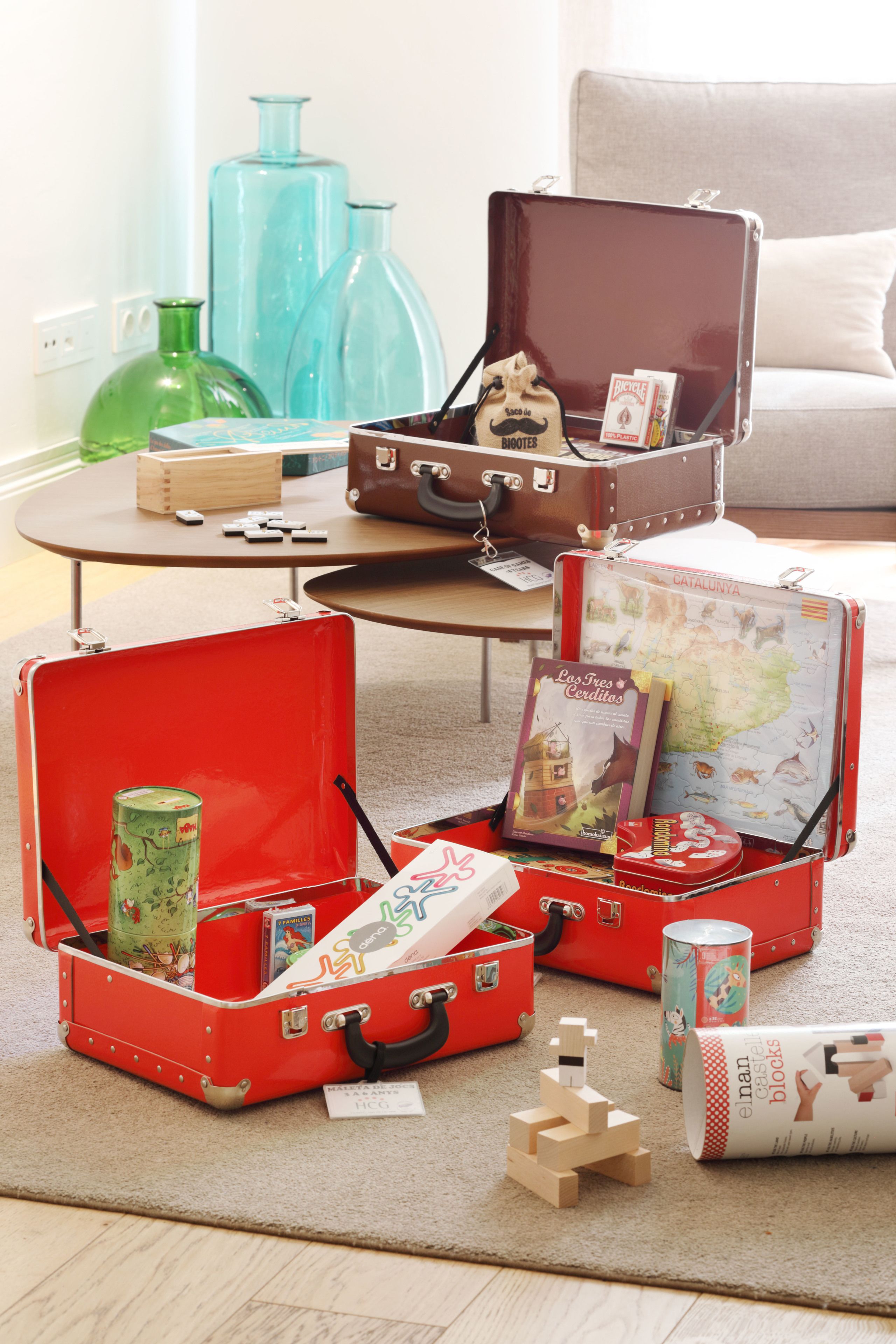 A room with a coffee table, two open suitcases, and various items on the floor.