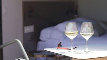 Two glasses of white wine on a white table in a hotel room with a bed in the background.