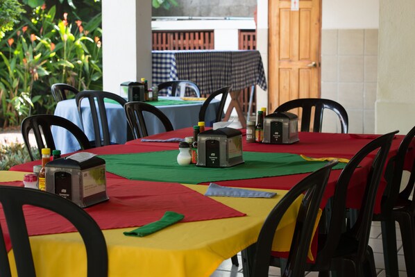 A dining area with tables covered in red and yellow tablecloths, black chairs, and condiments on the tables.