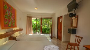 A hotel room with two beds, a TV, a chair, and a view of a garden through a sliding door. - Hotel Pochote Grande (Jacó)