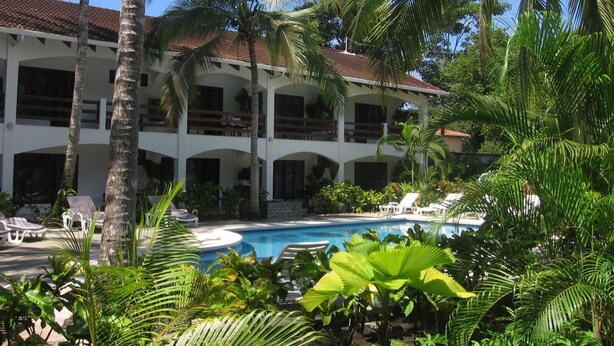 A resort with a pool, palm trees, and a two-story building with balconies. - Hotel Pochote Grande (Jacó)