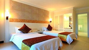 Een hotelkamer met twee bedden, een groot hoofdeinde, bedlampjes en een badkamer door een open deur zichtbaar.
