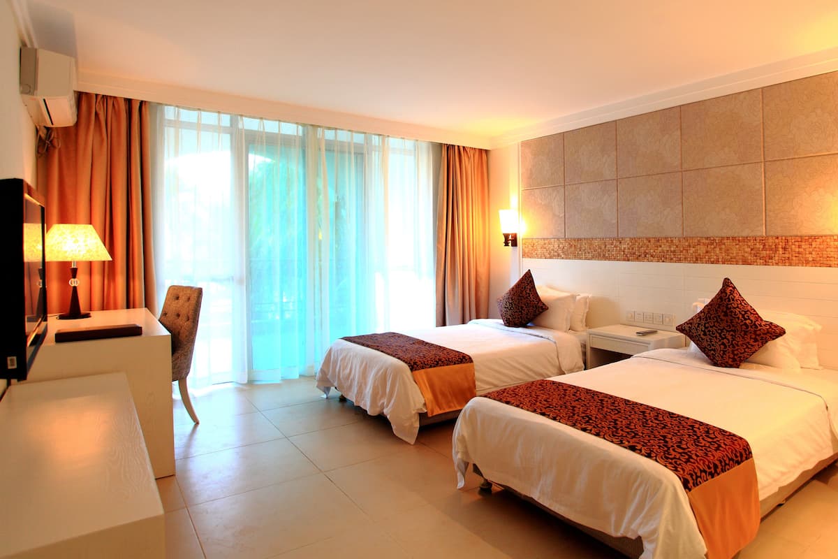A hotel room with two beds, a desk, a chair, and a window with curtains.
