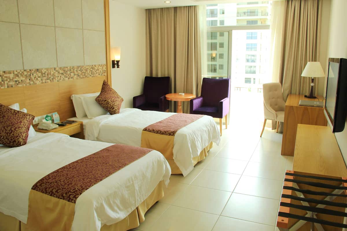 A hotel room with two beds, a desk with a TV, a chair, and a small table.