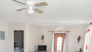 A spacious room with a dining table, chairs, a ceiling fan, a television, and a bed. - Clearwater Apartments (Oistins)