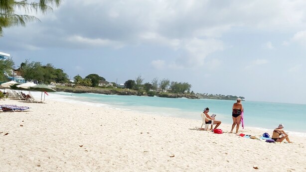 A beach with white sand, a few people, and umbrellas. - Clearwater Apartments (Oistins)