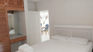 A bedroom with a bed, a wooden wardrobe, and a mirror. - Clearwater Apartments (Oistins)