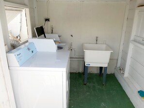 Un baño pequeño con un lavamanos blanco, una lavadora Whirlpool y piso verde.