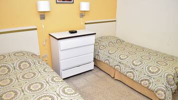 Una habitación con dos camas individuales, una mesita de noche blanca con lámpara y un edredón estampado.