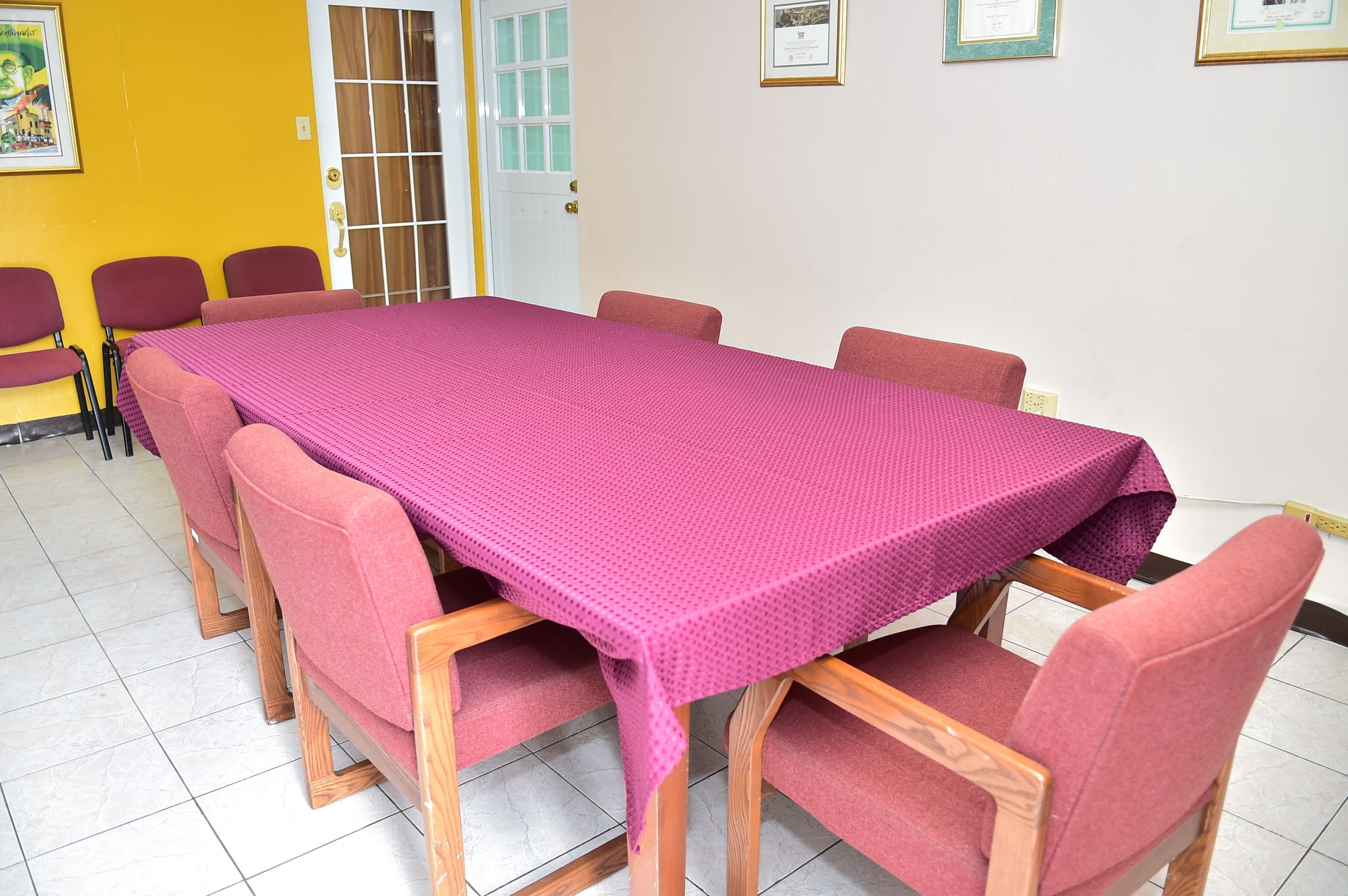 Une salle de conférence avec une longue table et six chaises, une porte et des certificats encadrés accrochés au mur.