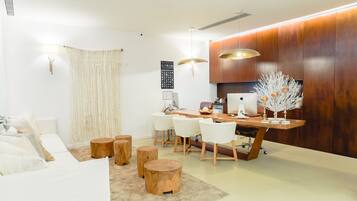 A modern living room with a sofa, wooden stools, a dining table with chairs, and a decorative tree.