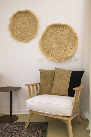 Una habitación con una silla de madera con cojín blanco, dos tapices tejidos, una mesita redonda y una alfombra texturizada.