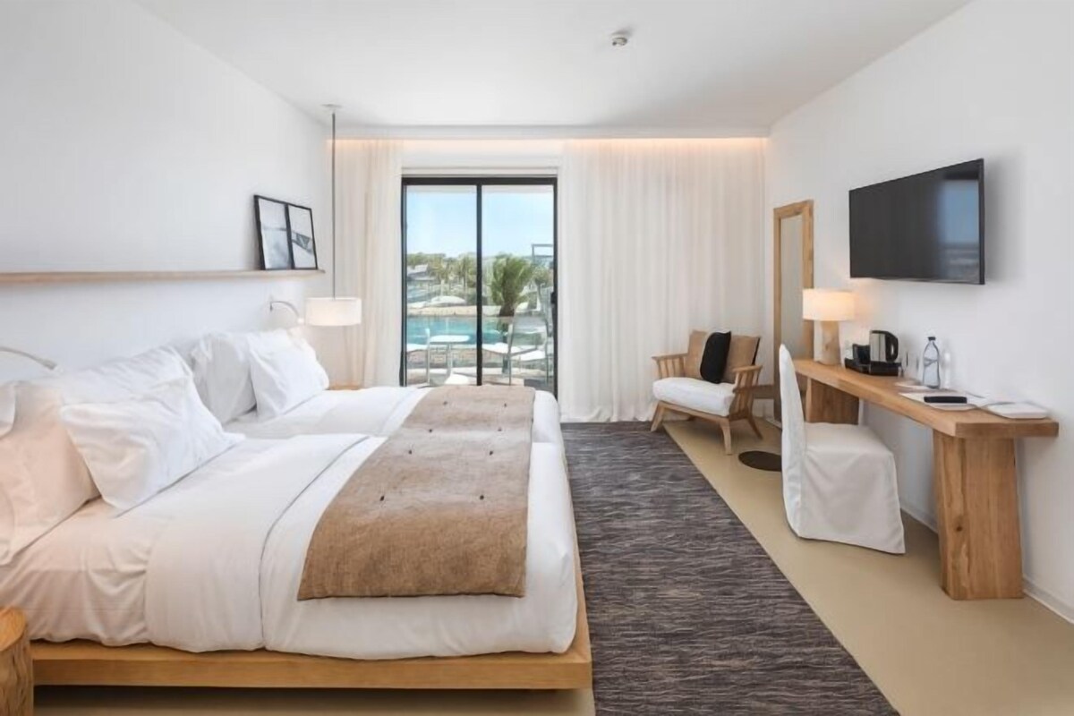 A hotel room with a bed, a desk, a chair, a TV, and a view of a pool.