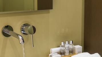 Une salle de bain avec un lavabo blanc, des robinets chromés, un miroir et des articles de toilette disposés sur une petite étagère.