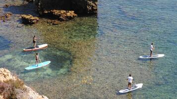 Three people paddleboarding on clear water near rocky shores.