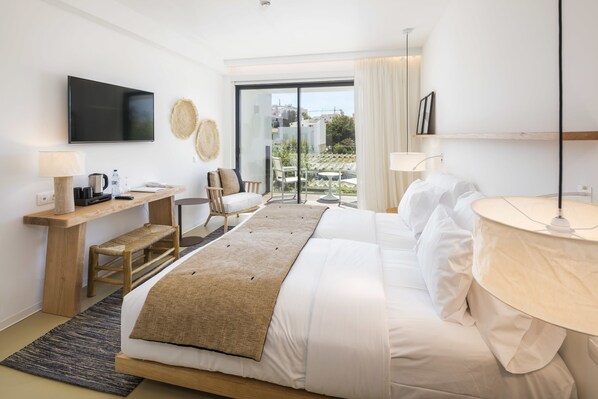 A modern hotel room with a large bed, a desk, a chair, a TV, and a balcony with a view of the city.