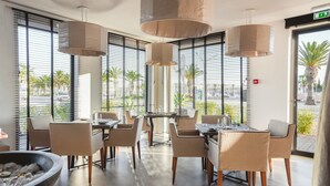 A modern dining area with large windows, multiple tables, and hanging pendant lights. - Lagos Avenida Hotel (Lagos)