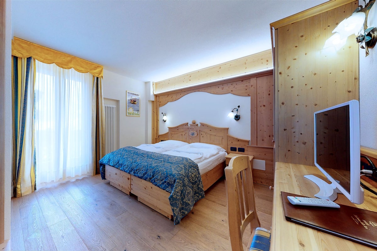 Une chambre à coucher avec un cadre en bois, comprenant un lit, un bureau avec un ordinateur et un téléviseur.