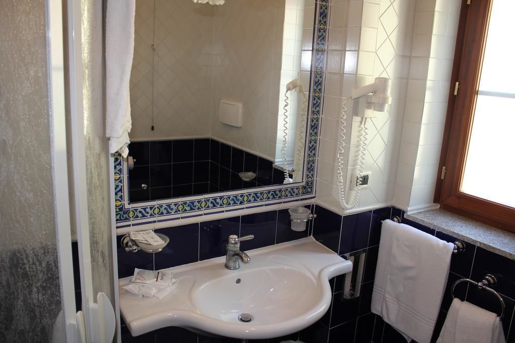 Un bagno con un lavandino bianco, uno specchio e una finestra con un portasciugamani.