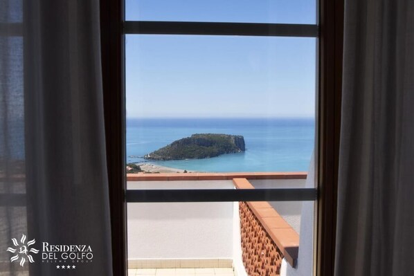 A view from a window of a building overlooking a coastal area with a small island and beach. - Hotel Residenza del Golfo (Praia a Mare)