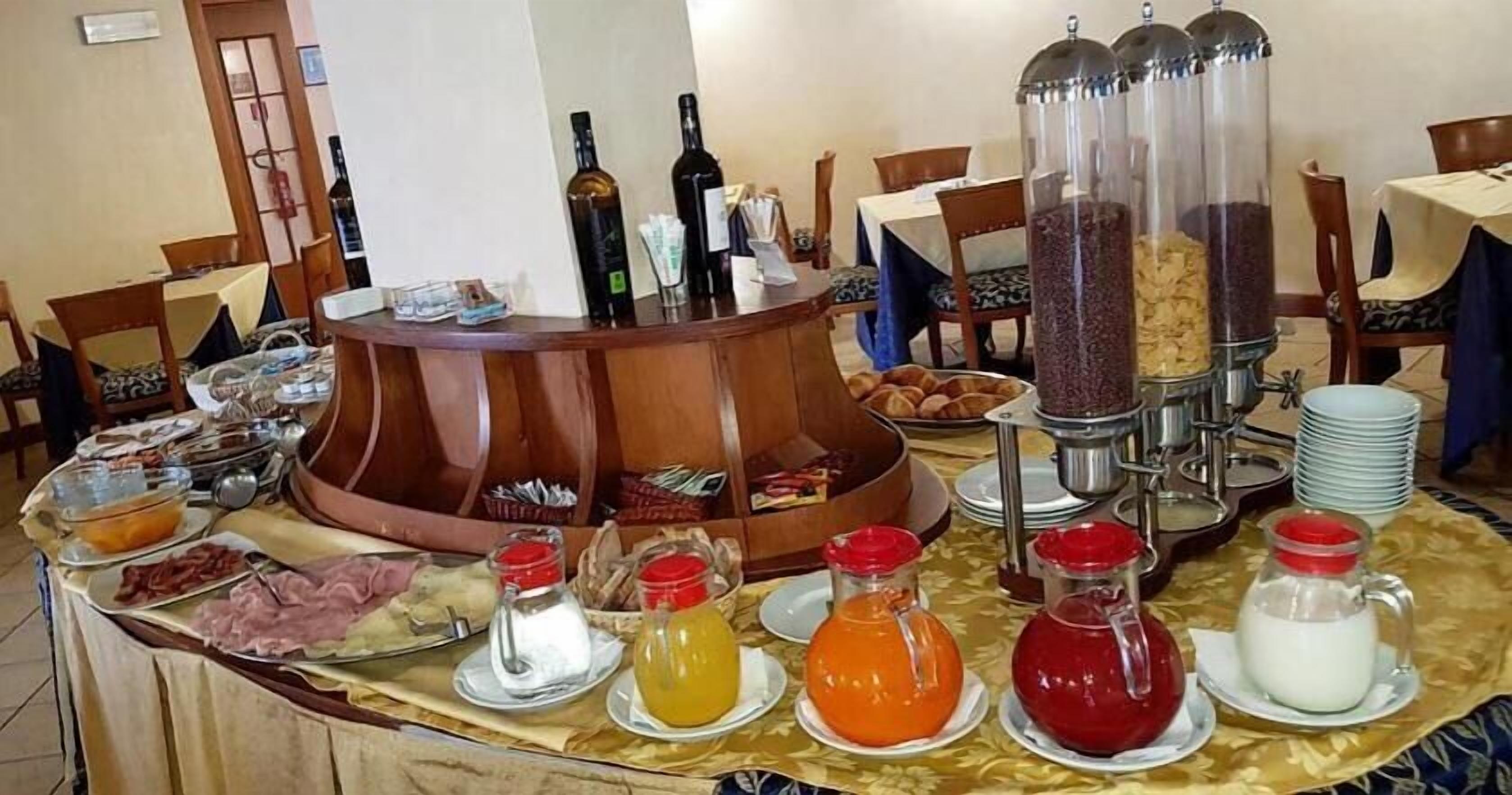 Un bufé de desayuno con diversos alimentos y bebidas, incluyendo tarros de mermelada, una máquina de café y botellas de aceite de oliva.