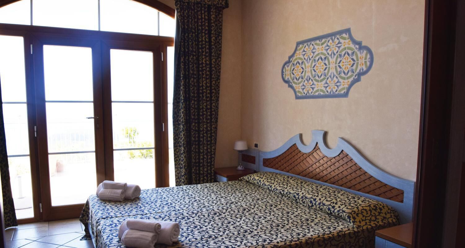 Un dormitorio con una colcha estampada, un adorno en la pared y vistas a través de un ventanal.