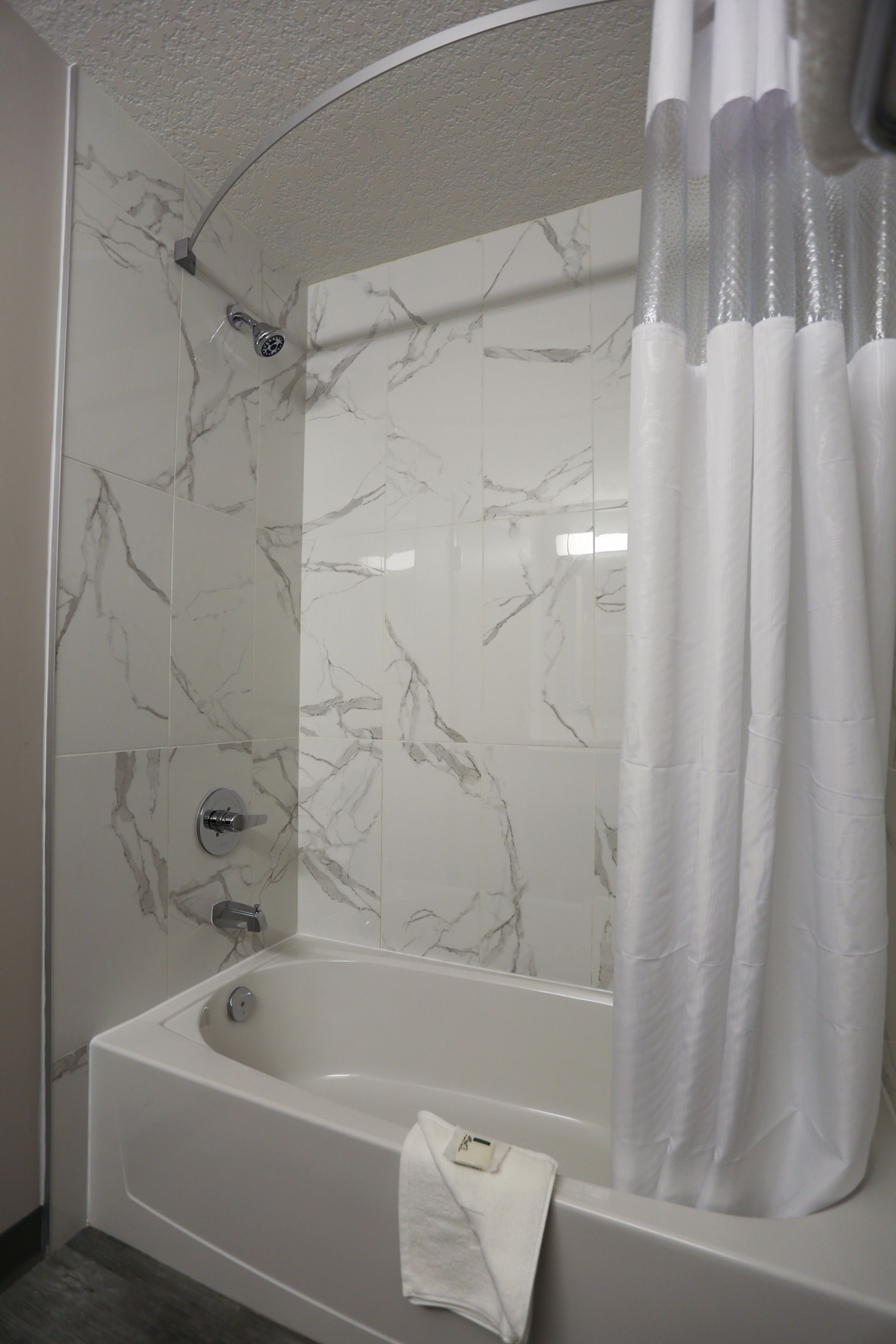 Ein modernes Badezimmer mit einer Duschwand aus Marmor, einer weißen Badewanne und einer Duschvorhang.
