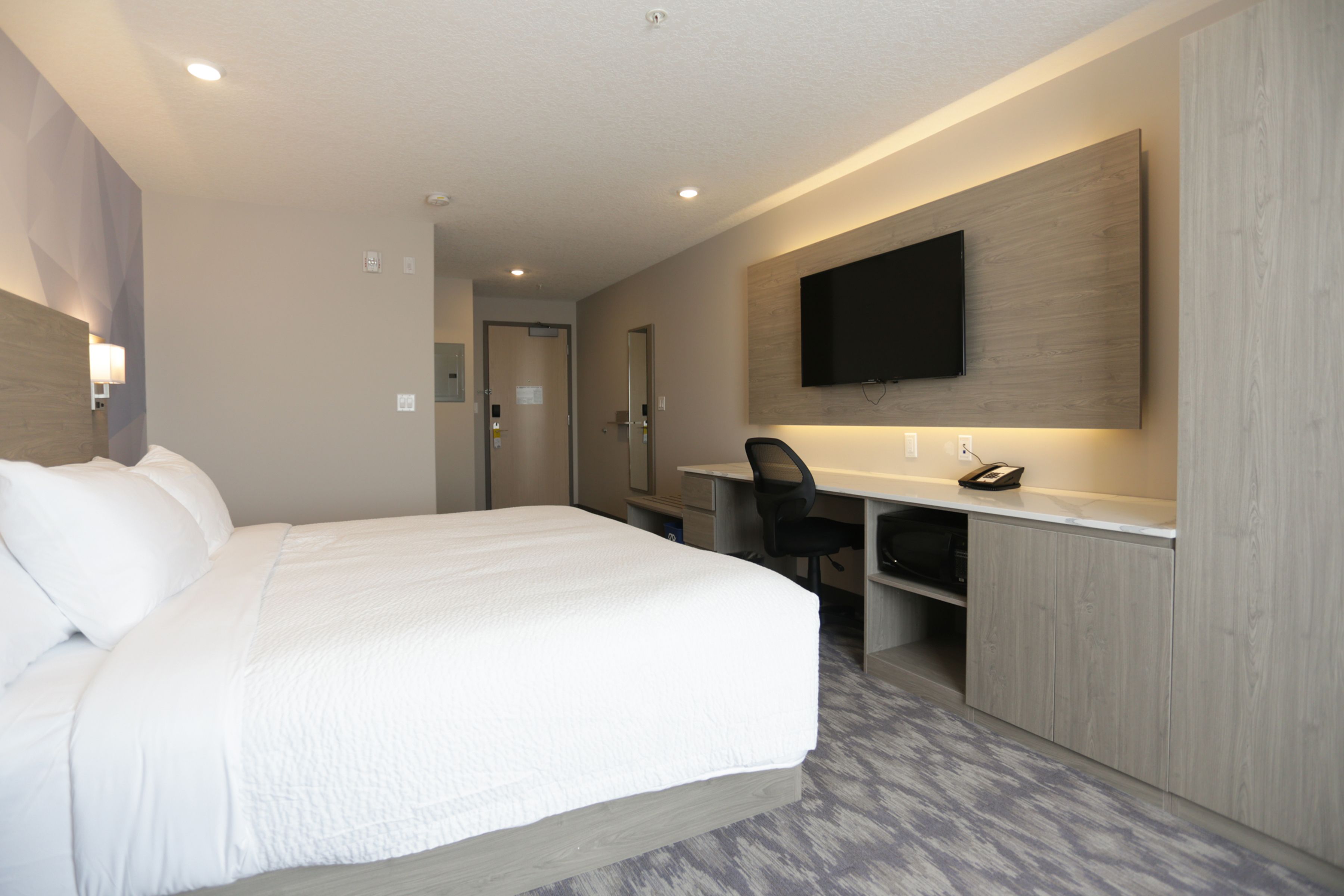 Habitación de hotel con una cama grande, un escritorio, una silla, un televisor de pantalla plana montado en la pared y una puerta que da al baño.