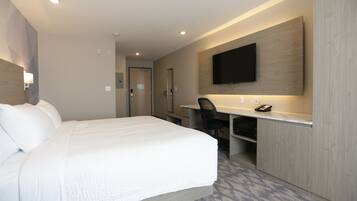 Habitación de hotel con una cama grande, un escritorio, una silla, un televisor de pantalla plana montado en la pared y una puerta que da al baño.