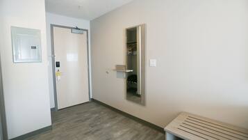 A hallway with a wooden floor, a bench, a door with a light switch, and a mirror on the wall.