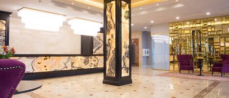 A lobby with a marble reception desk, a tall pillar, and purple seating.