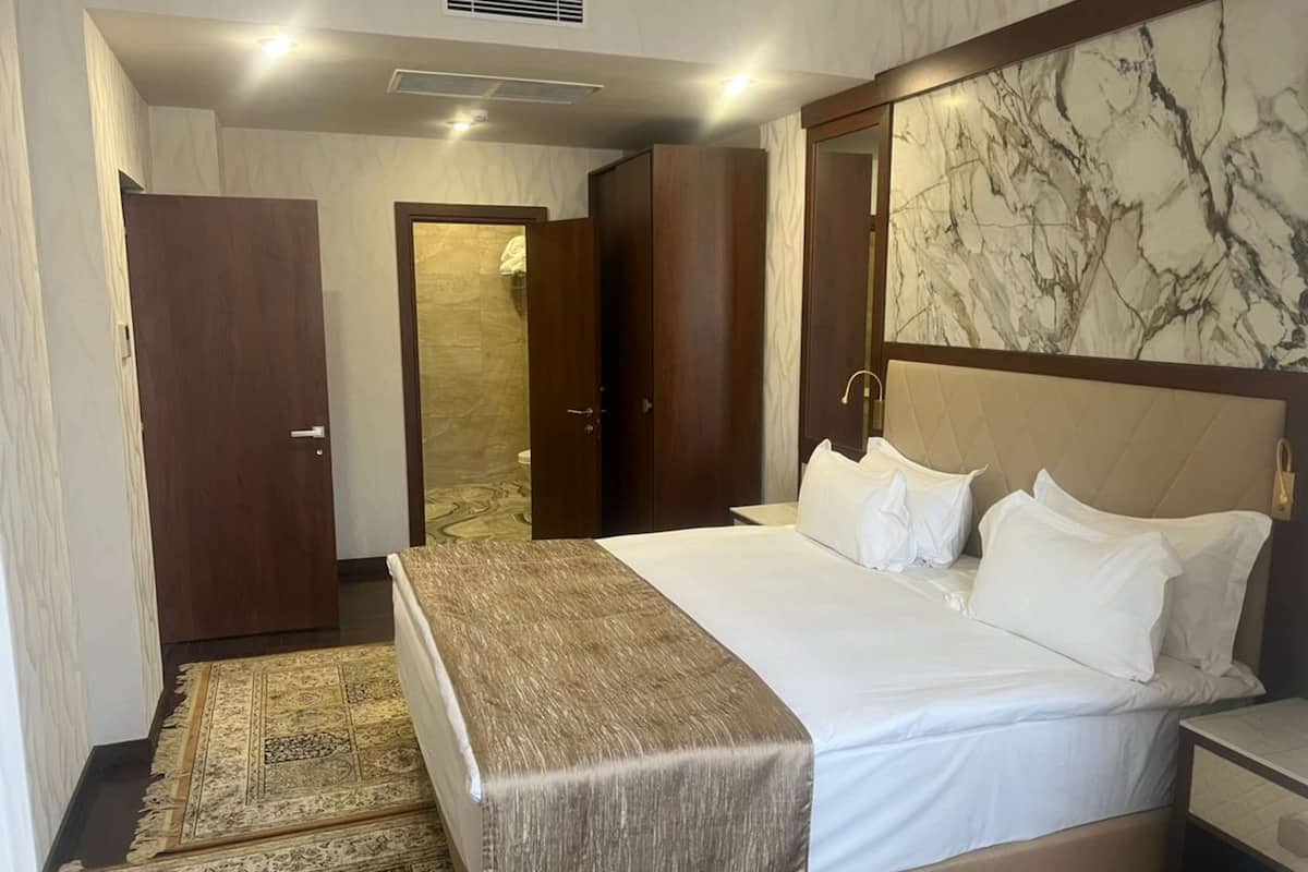 A hotel room with a large bed, wooden wardrobe, and a marble wall.