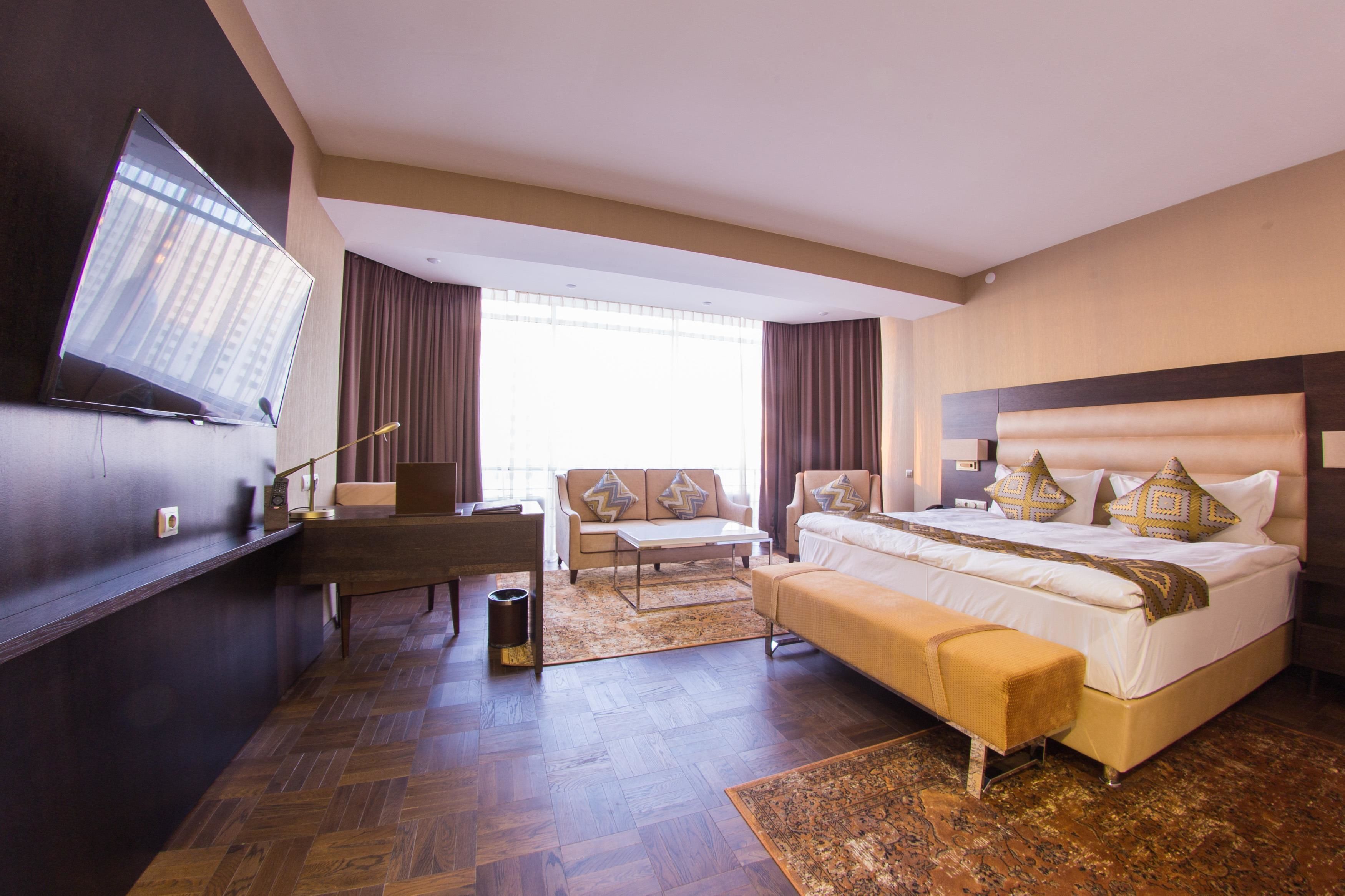 A hotel room with a large bed, a sofa, a desk, and a TV mounted on the wall.
