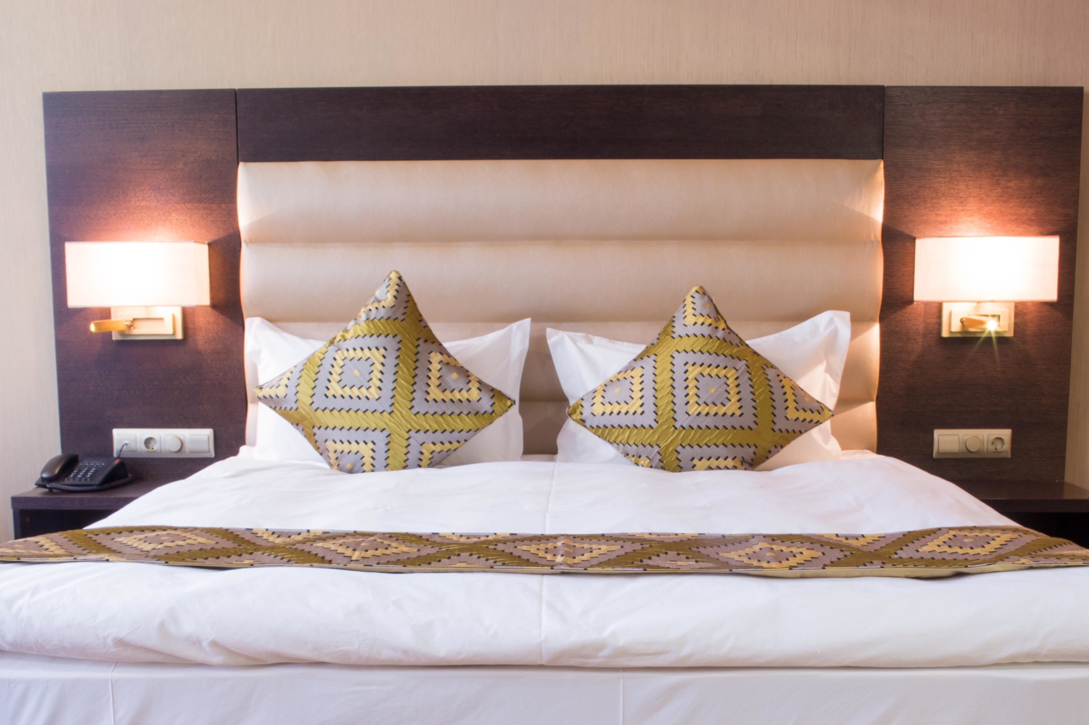 A neatly made bed with a patterned bedspread, two decorative pillows, and two wall-mounted lamps on either side.