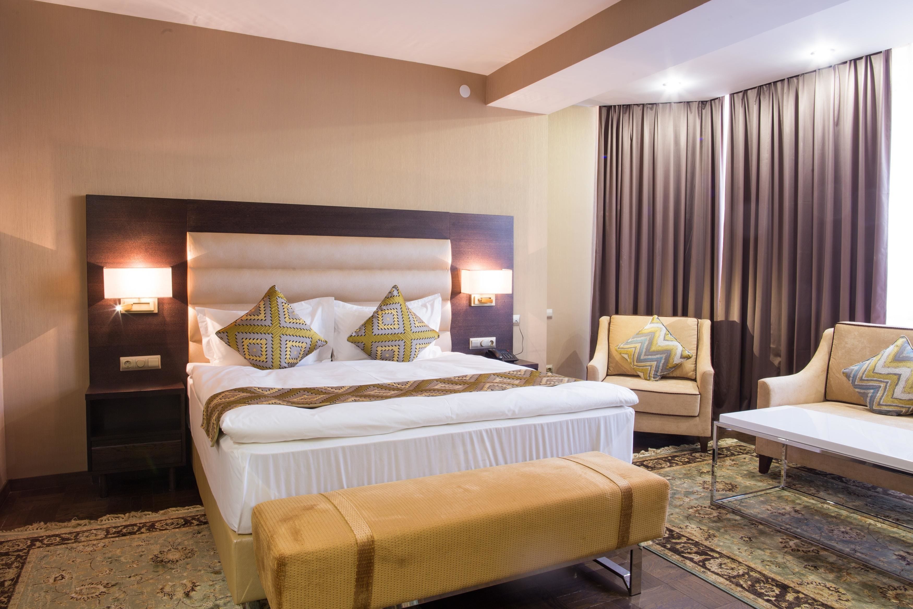 Una habitación de hotel con una cama grande, dos lámparas de noche, un sofá y una silla.