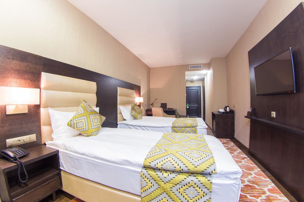 A hotel room with two beds, a TV, a desk with a phone, and a mirror.