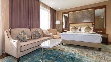 A hotel room with a bed, two sofas, a small table, a lamp, and a large mirror.