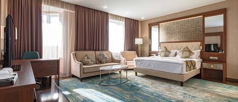 Una habitación de hotel con cama, escritorio, sillón, sofá y un gran ventanal con cortinas.