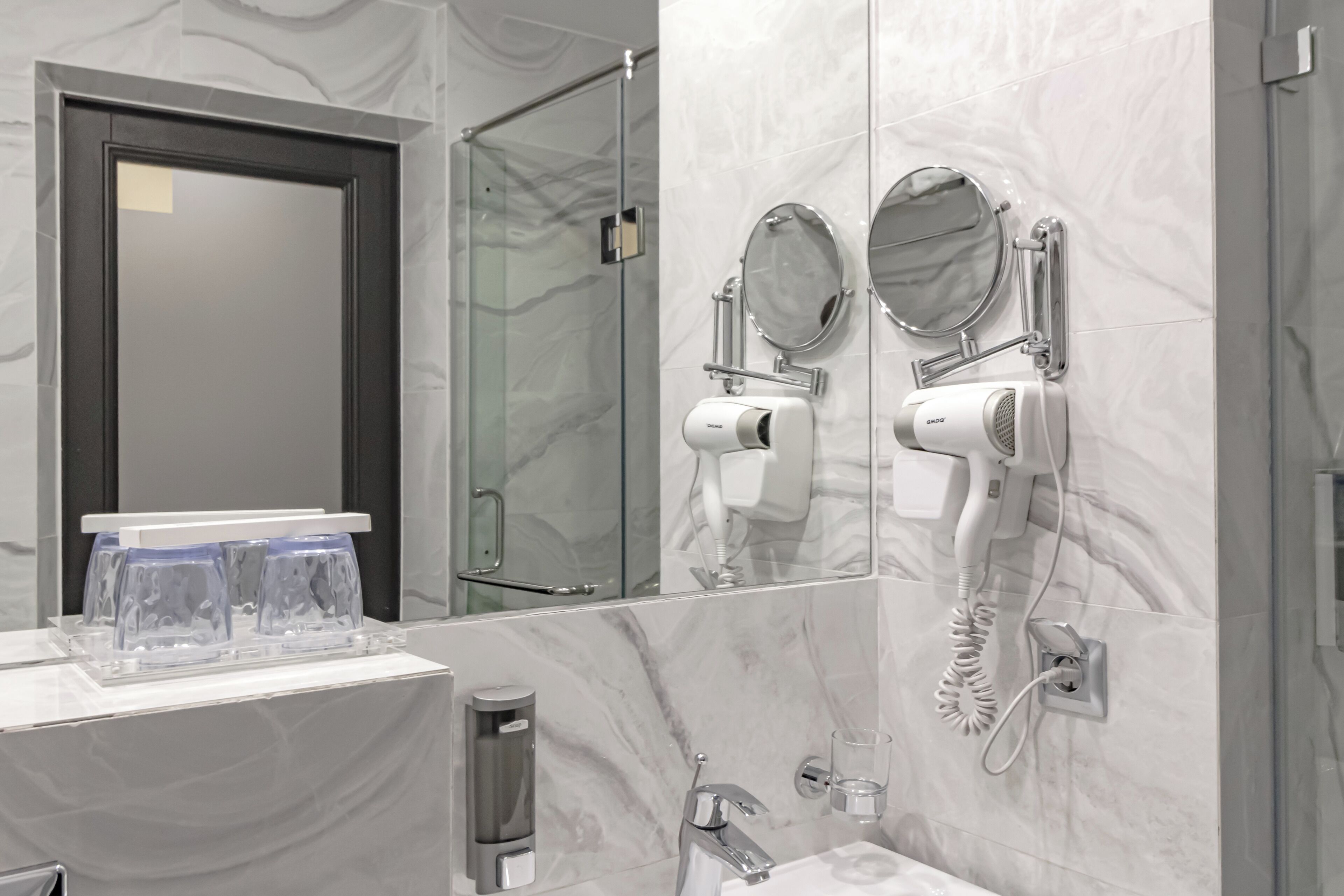 A bathroom with a marble wall, a sink with a towel dispenser, and two hair dryers mounted on the wall.