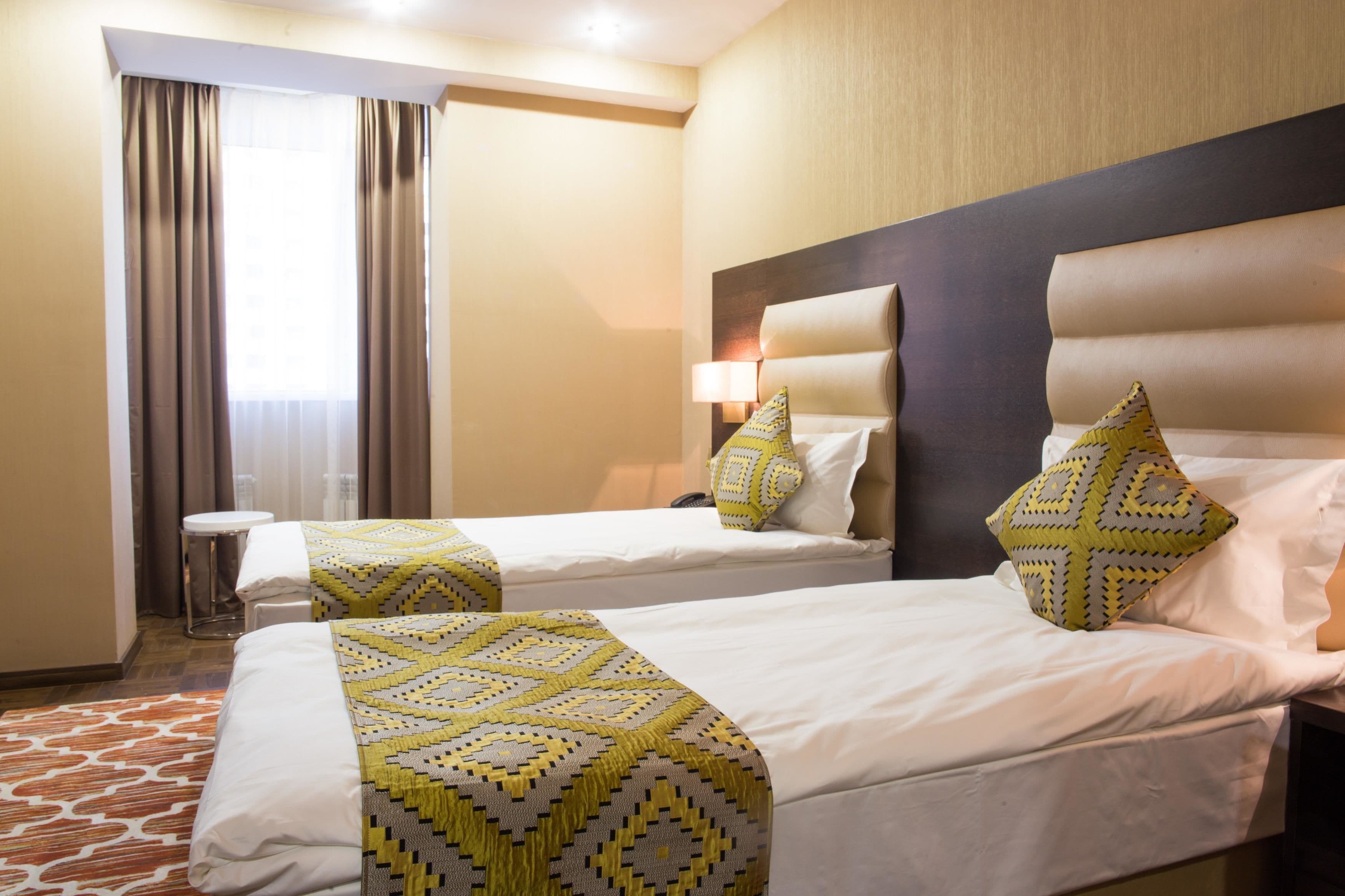 Habitació d'hotel amb dos llits, una tauleta de nit, una làmpada i una finestra amb cortines.