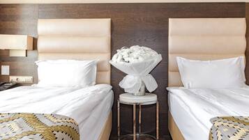 A hotel room with two beds, a small side table, a vase of flowers, and a wall-mounted lamp.