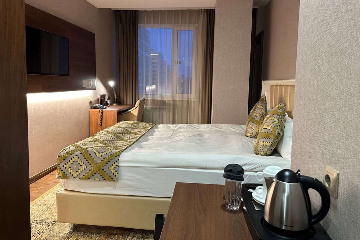 A hotel room with a bed, a desk, a coffee maker, and a TV on the wall.