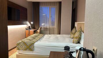 Een hotelkamer met een bed, een bureau, een koffiezetapparaat en een televisie aan de muur.