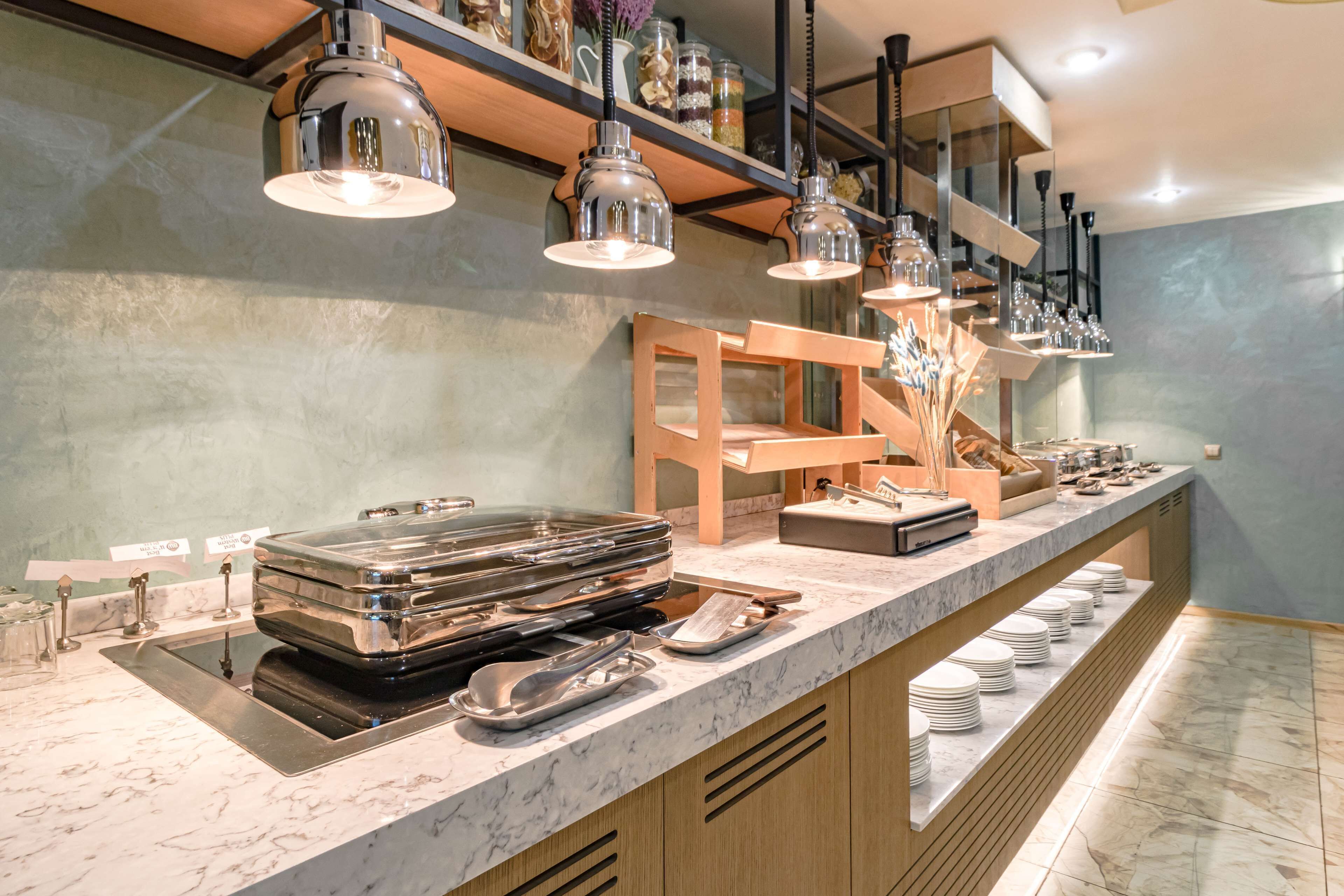A buffet setup with stainless steel serving trays, a wooden chair, and a marble countertop.