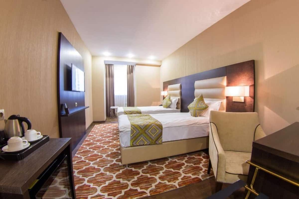 A hotel room with a bed, bedside tables, a desk, a chair, a TV, and a bathroom visible through a door.