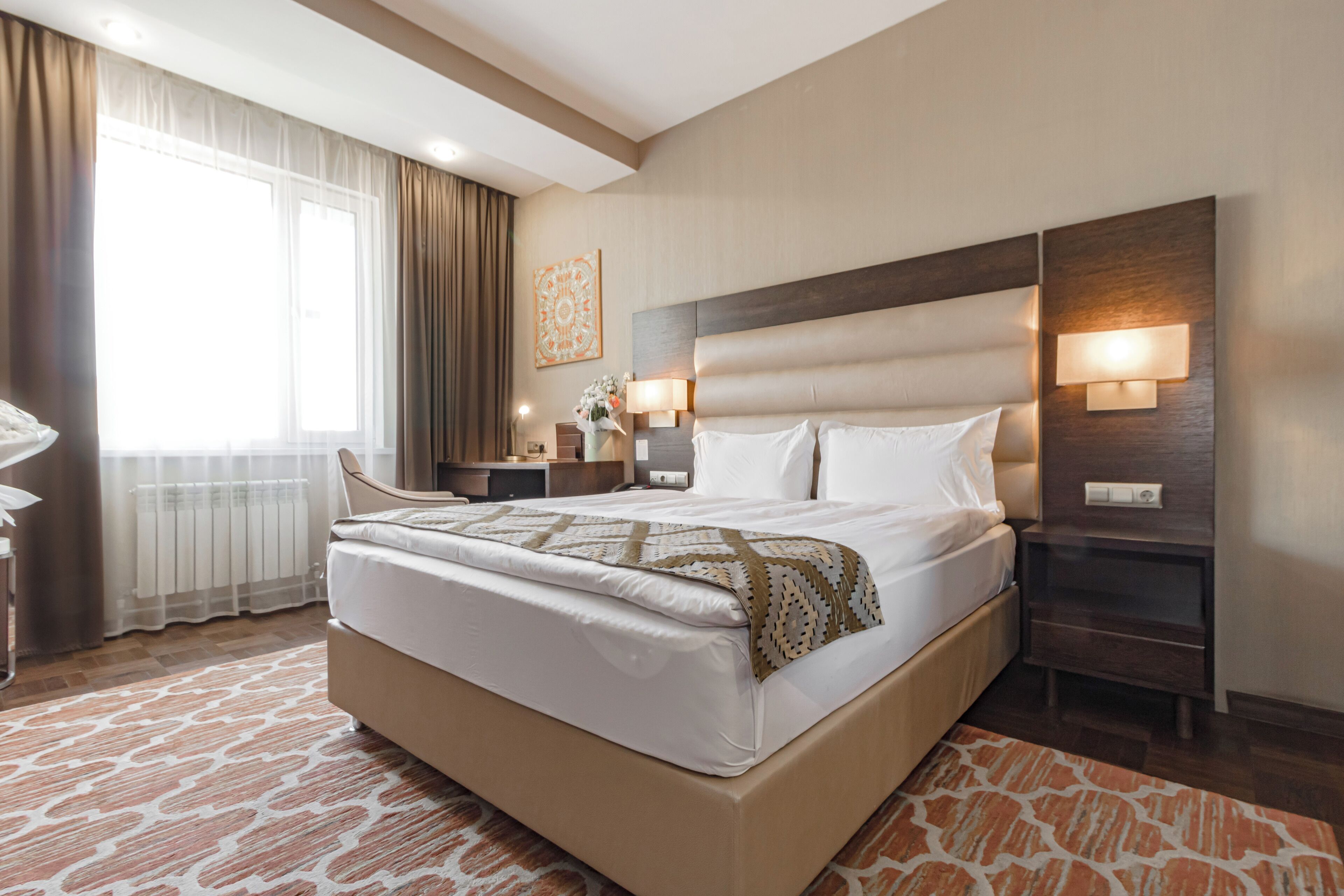 A hotel room with a large bed, bedside tables, a nightstand, a lamp, and a window with curtains.