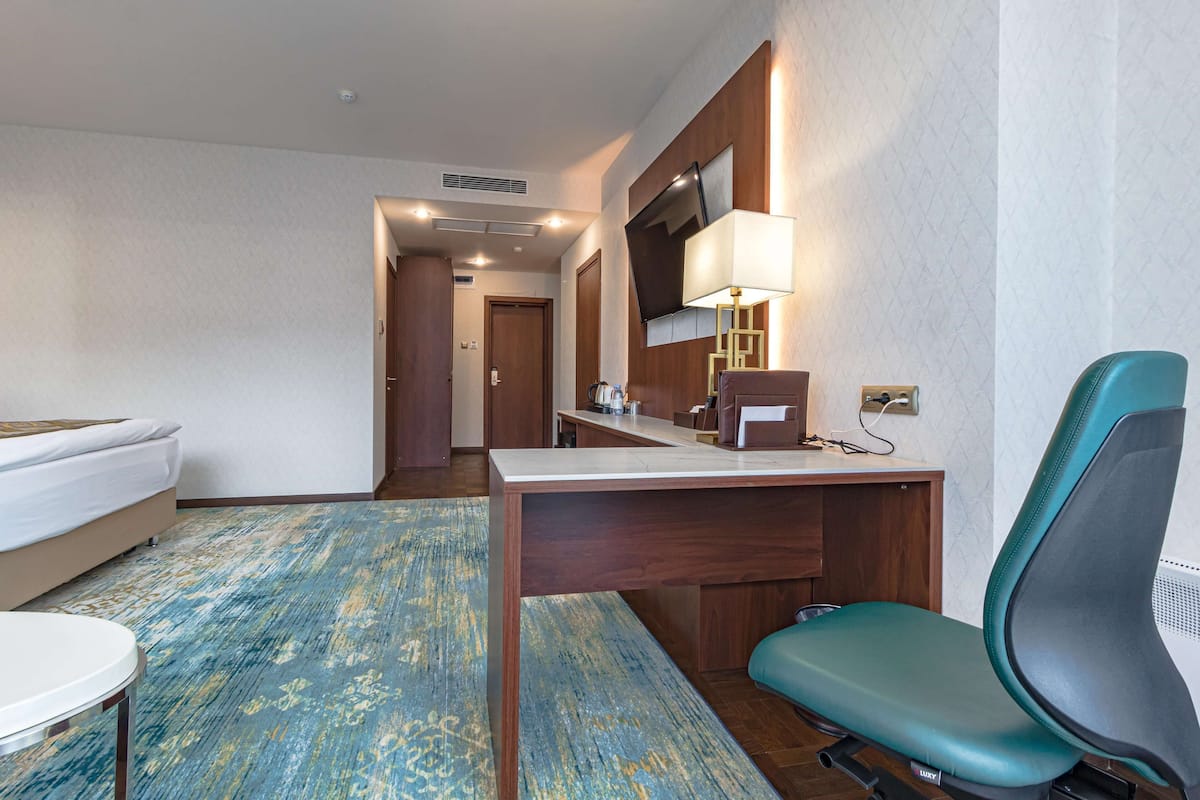 A hotel room with a bed, desk, chair, and a TV mounted on the wall.