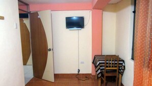 A small room with a television mounted on the wall, a wooden chair, and a tiled floor. - Hostal Ayllu (Urubamba)