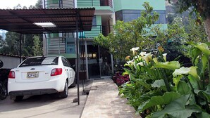 A white car parked in front of a multi-story building with a green facade and a covered parking area. - Hostal Ayllu (Urubamba)